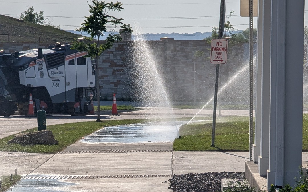 Sprinkler spraying across the sidewalk and street in downtown Superior, Colorado, with paving equipment in the background